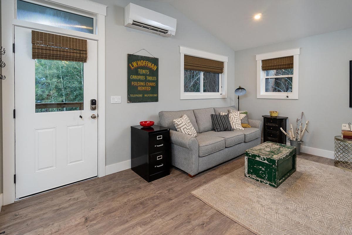 Cozy living room with a grey sofa, black file cabinet, and a distressed green coffee table. A white door opens to a view of trees.