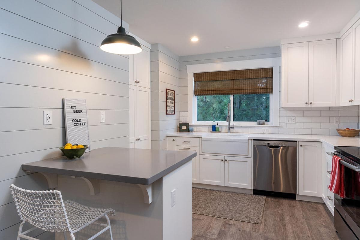 Bright, modern kitchen with white cabinets, a farmhouse sink, and a gray countertop bar. A pendant light illuminates the eating area.