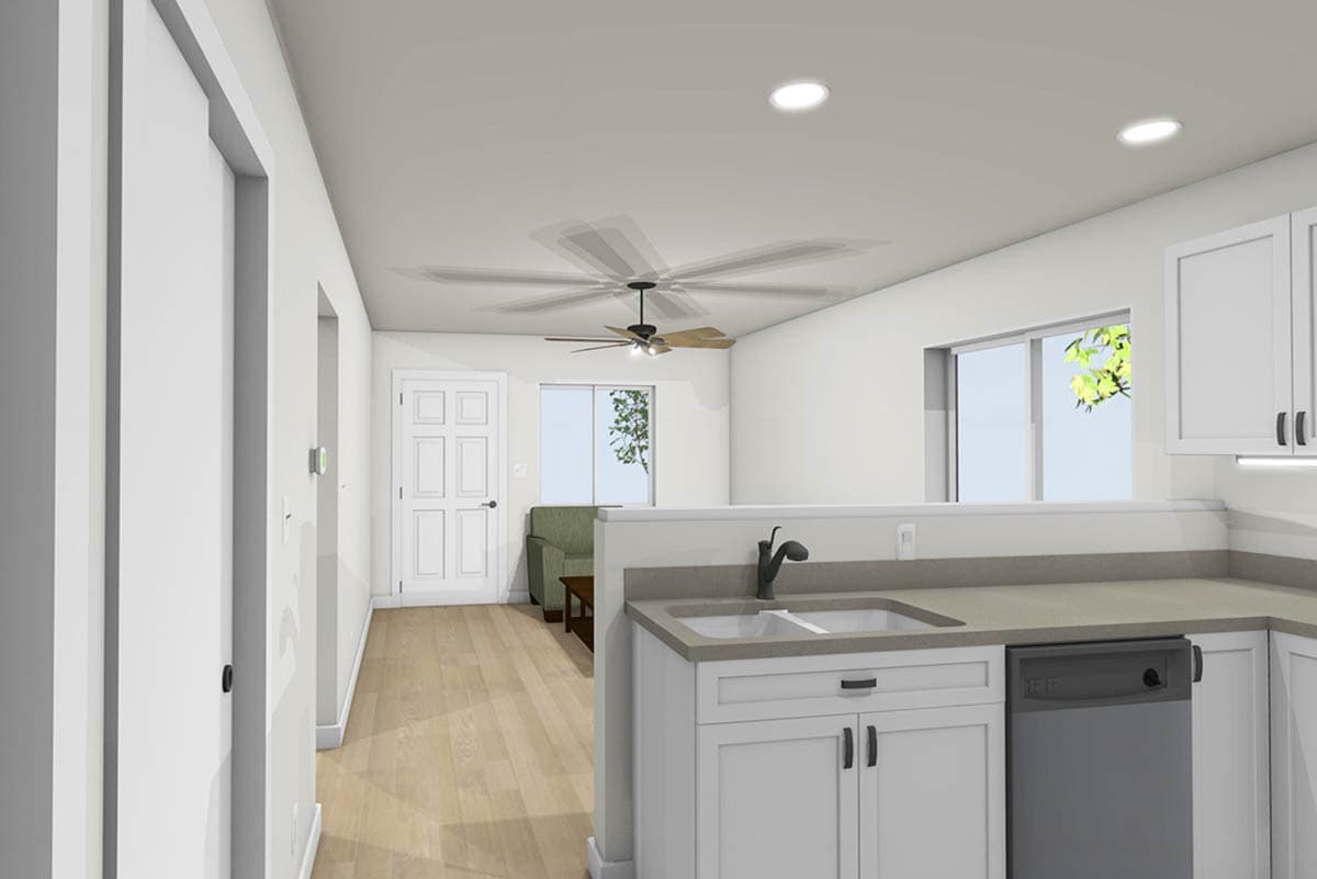 A bright, open-plan interior with kitchen cabinets, a sink, and a view into a living area with a sofa, all beneath a ceiling fan.