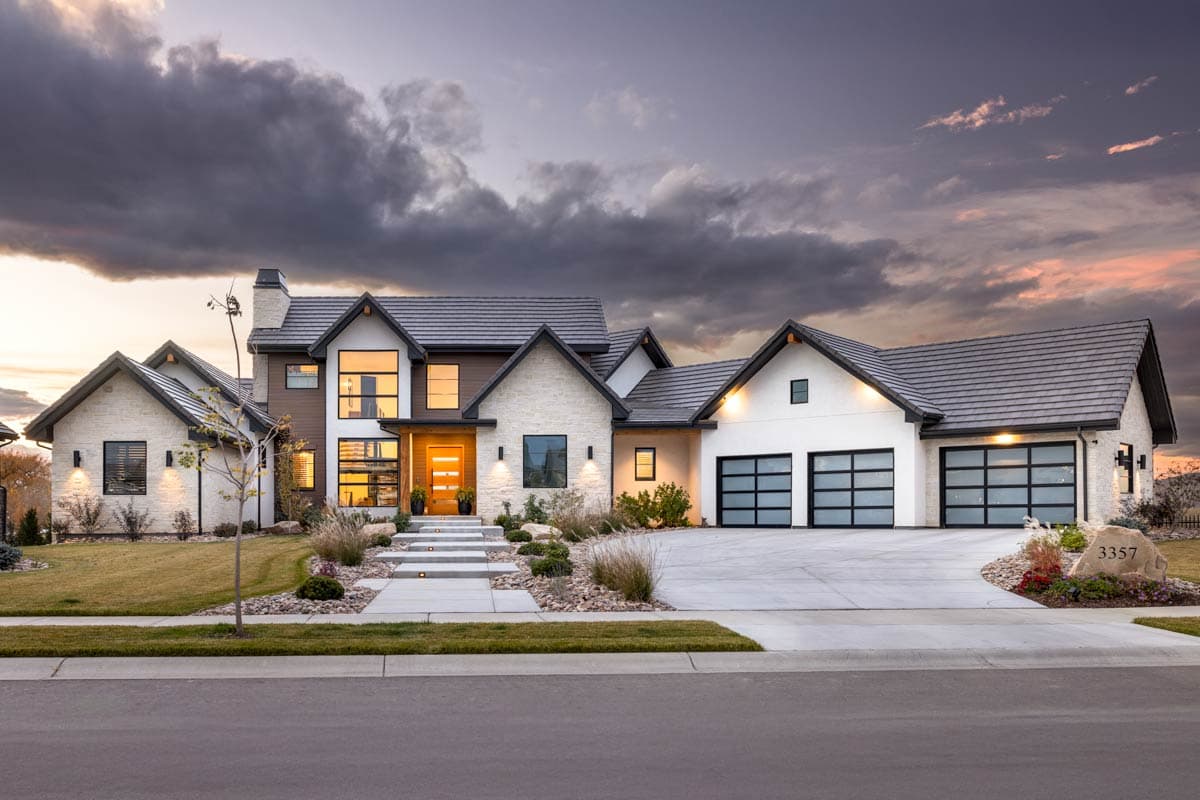 House plan exterior. Two-story Modern Farmhouse with gabled rooflines, stone facade, and a three-car garage. Features large windows and entry porch.