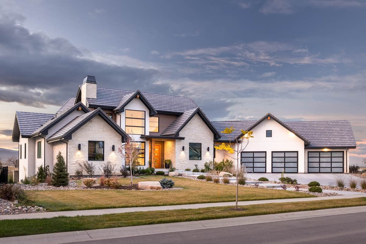 Modern house plan exterior with stone accents, large gables, a prominent chimney, and three glass garage doors.