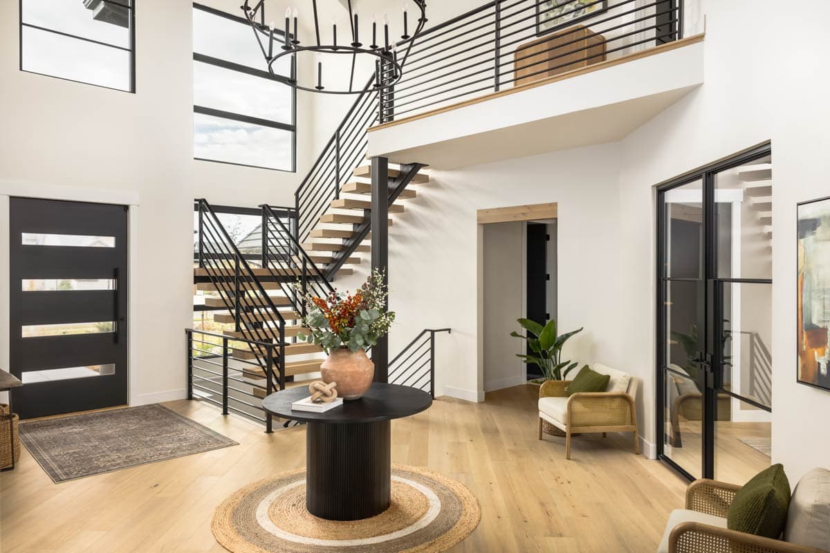 Modern house foyer with open-riser staircase, black metal railings, large windows, and double glass doors.