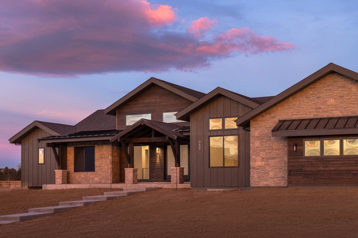 House plan exterior with stone and wood siding, multiple gables, covered entry, and dark metal rooflines.