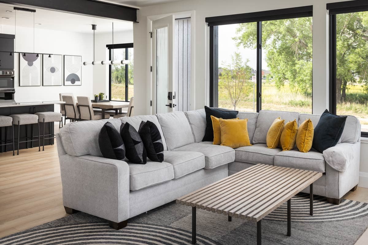 Living room with sectional sofa, coffee table, open to kitchen with island and dining area. Large windows.