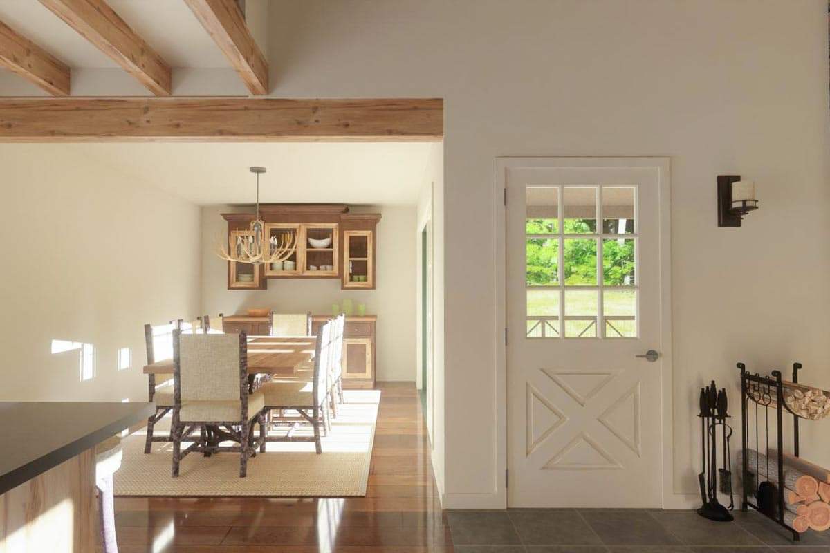 A rustic dining room with wooden beams and a table set for guests. A glass-paned door opens to a bright outdoor view.