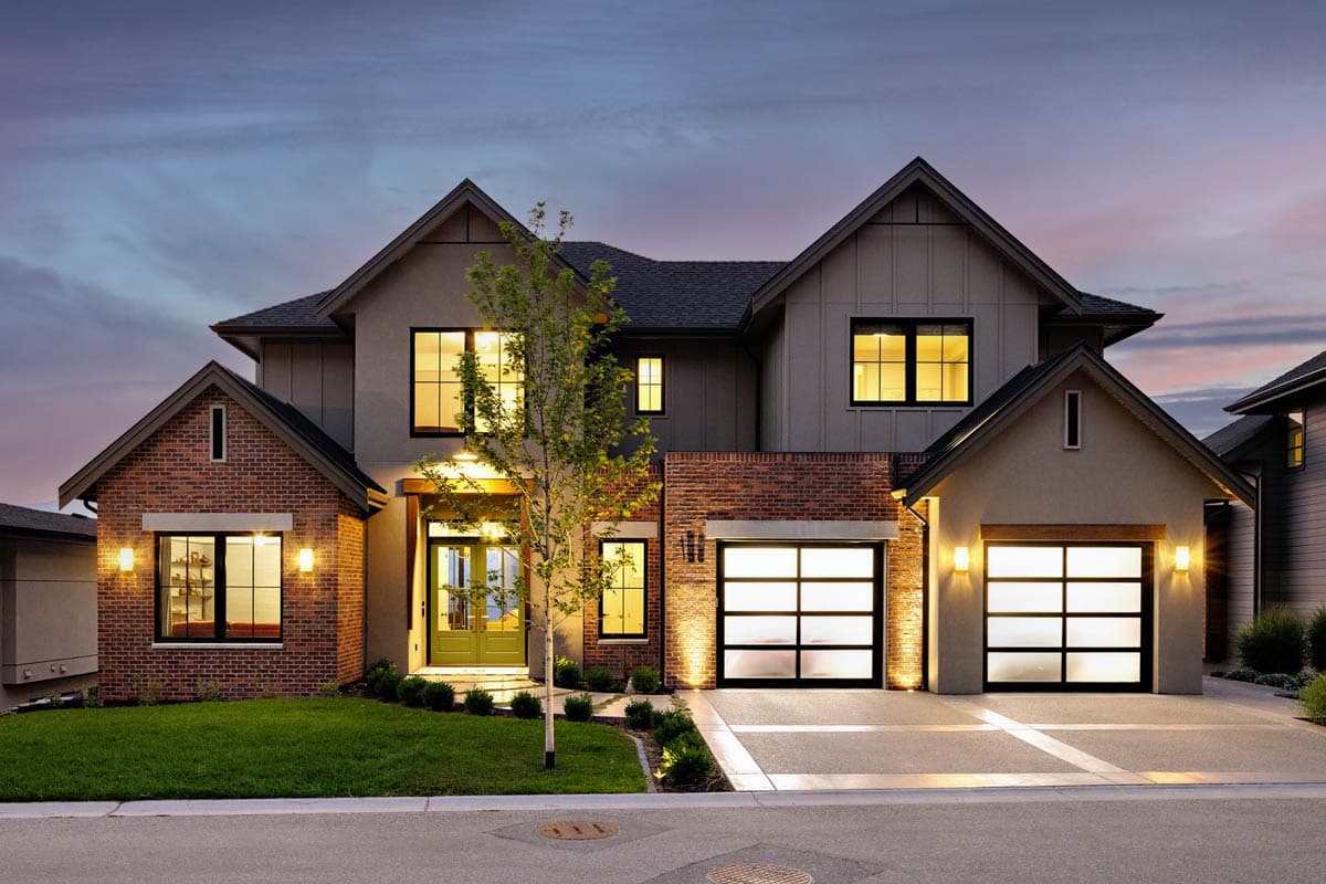 House plan exterior. Two-story home with a gabled roof, brick accents, and a front-facing garage with glass panel doors.