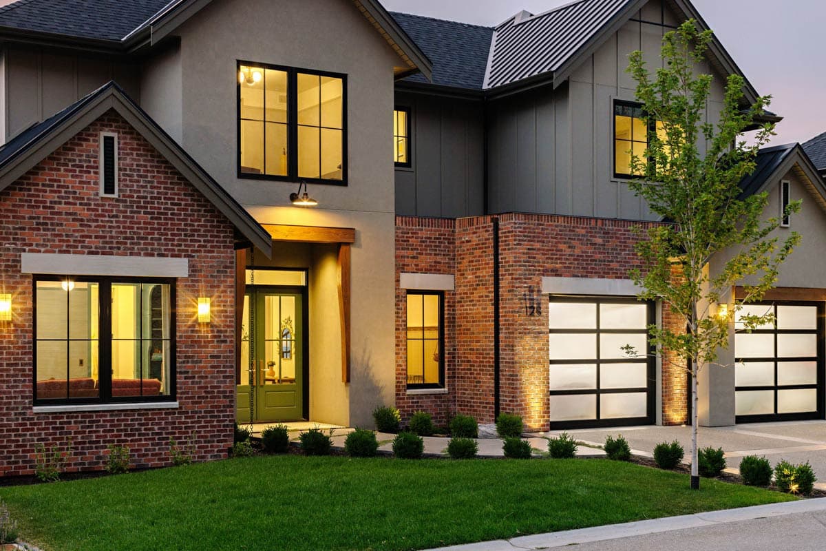 House plan exterior with brick and stucco facade, gabled roof, two-car garage with glass doors, and prominent entrance.