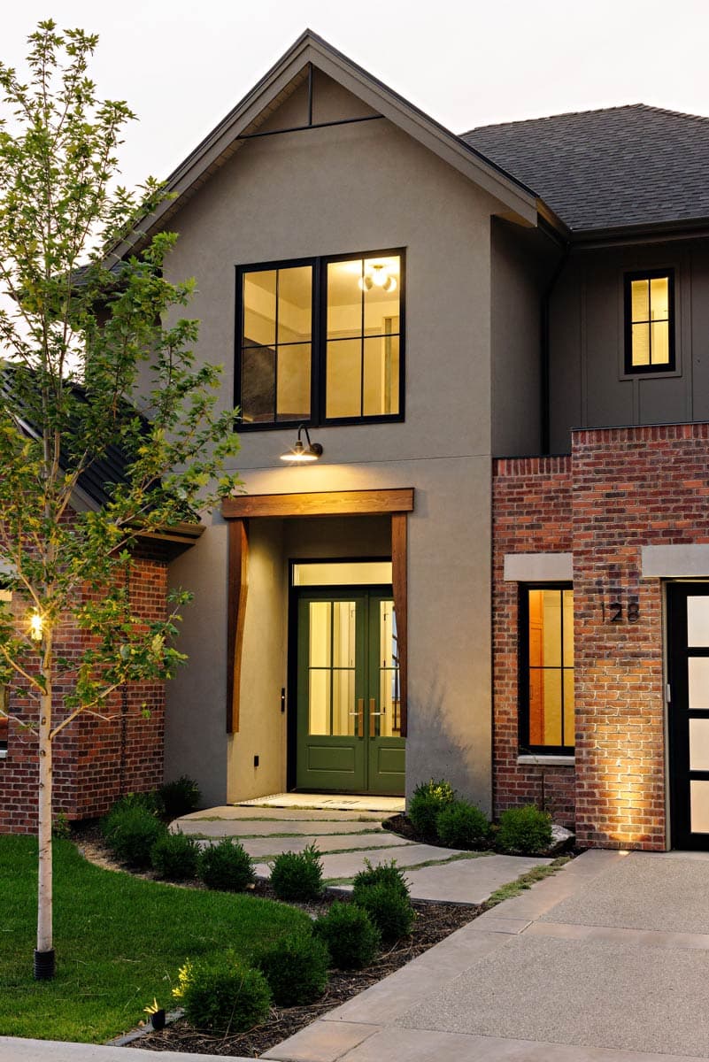 House plan exterior featuring a mix of stucco and brick, a prominent gable roofline, double entry doors, and large grid windows.