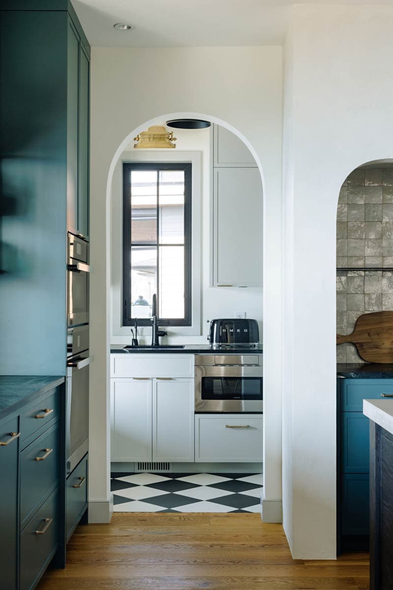Kitchen interior with arched entryway, dark cabinetry, stainless steel appliances, checkered tile floor, and window with black grid.