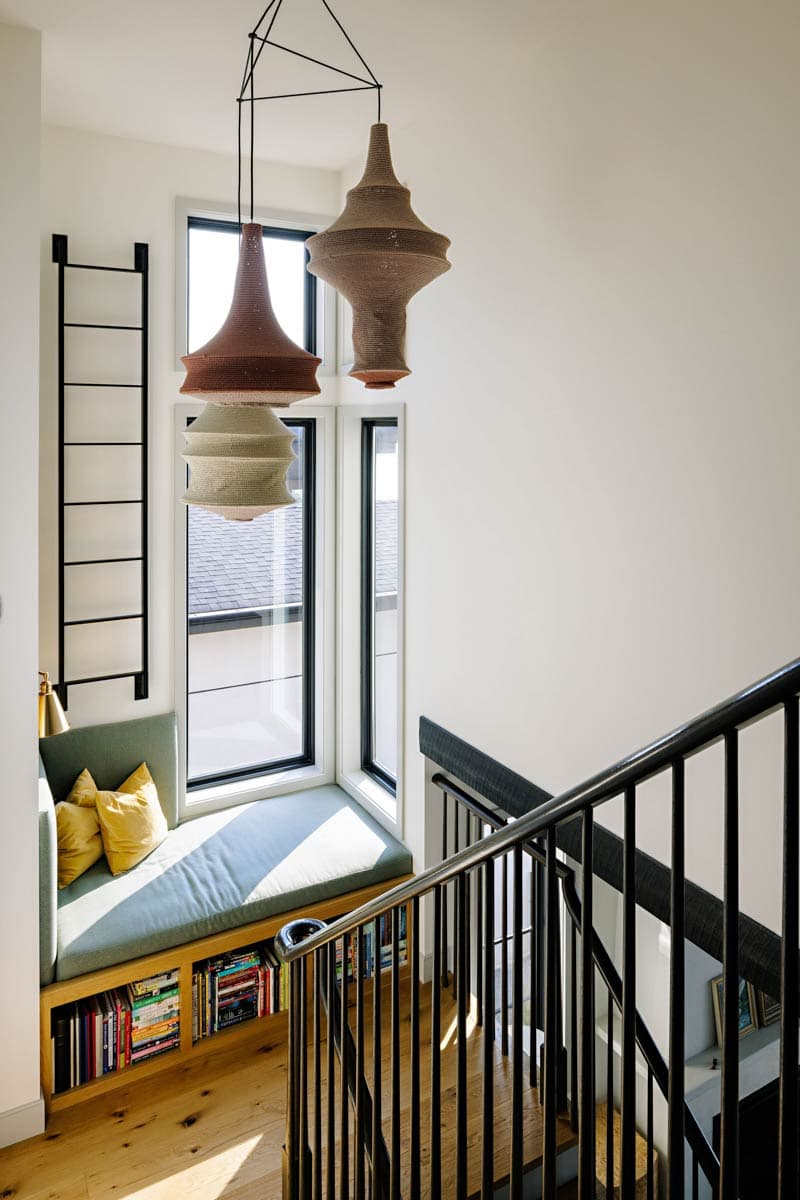 Interior view of staircase landing with built-in bench seating and bookshelves, bay window, and decorative pendant lights.