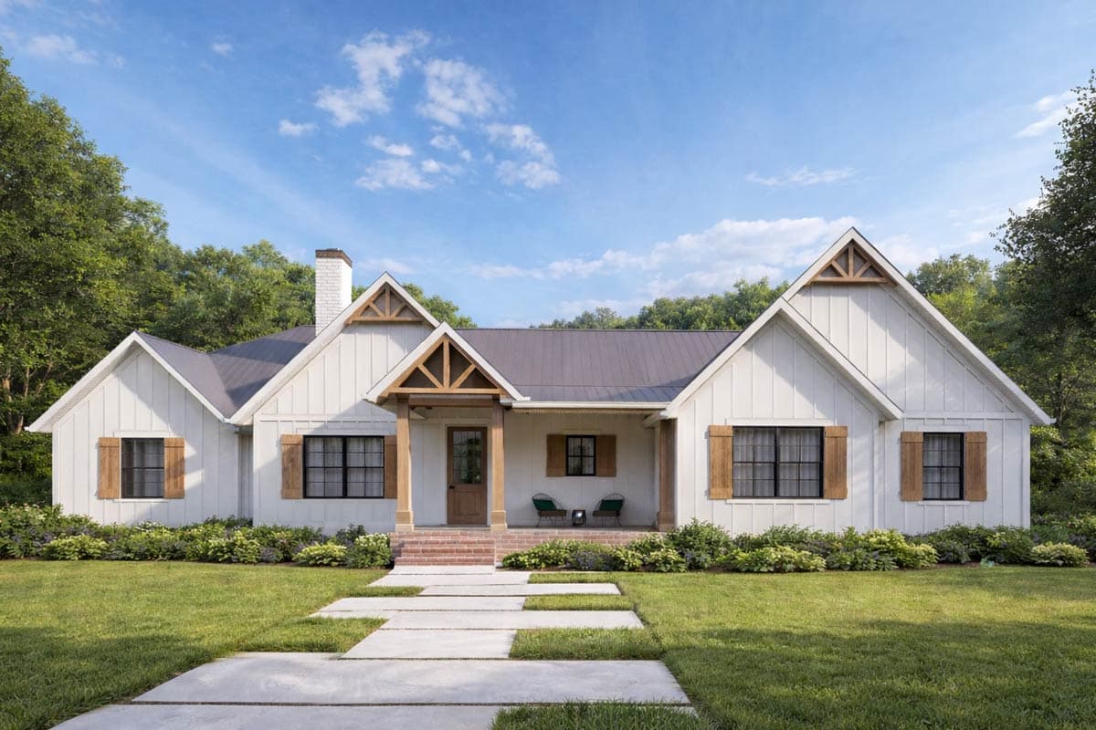 A white farmhouse with a dark metal roof, wood accents, and a porch. Green shrubs line the base, and a stone walkway leads to the front door.