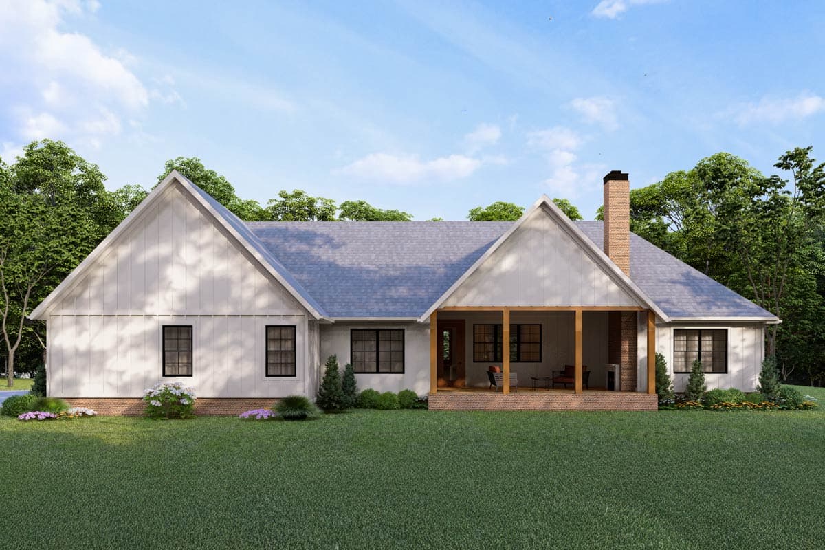 A white farmhouse with a gabled roof and a brick chimney. A covered porch faces a green lawn, and trees surround the house.