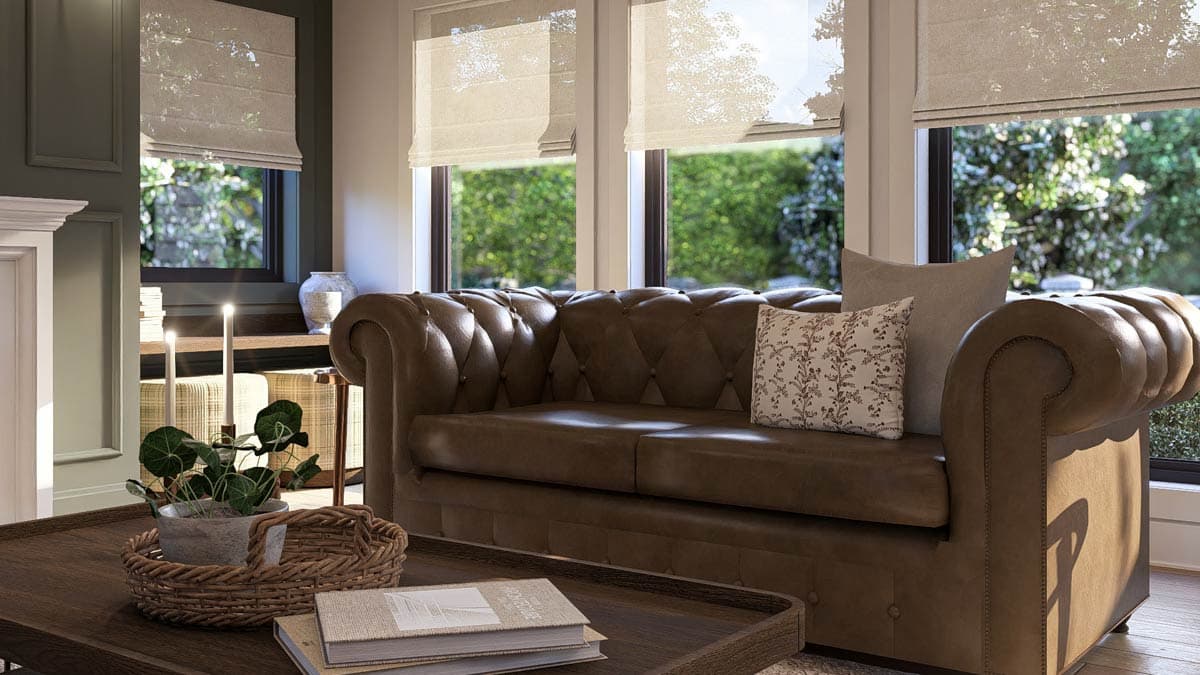 Living room interior with tufted brown leather sofa, dark wood coffee table, and large windows with Roman shades overlooking greenery.