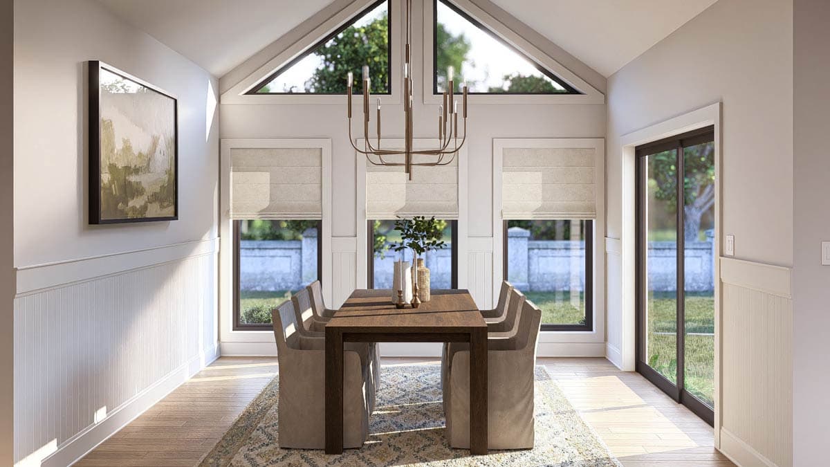Dining room with vaulted ceiling, large windows, sliding glass door, and wainscoting.
