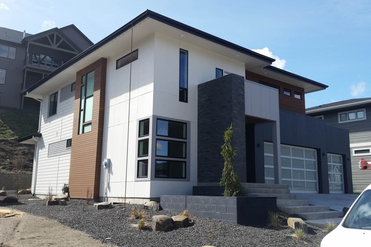 House plan exterior. Modern style, two-story home with flat roof. Features include a vertical accent panel, large windows, and a glass garage door.