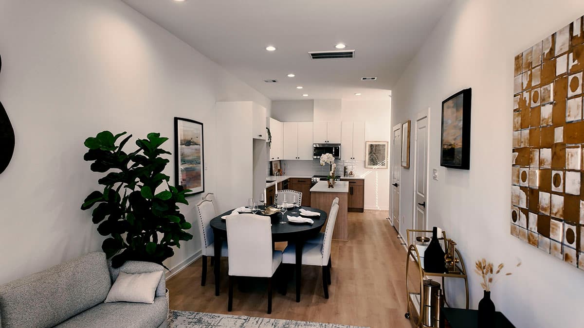 Open concept living and dining area adjacent to a modern kitchen with island and white cabinetry.