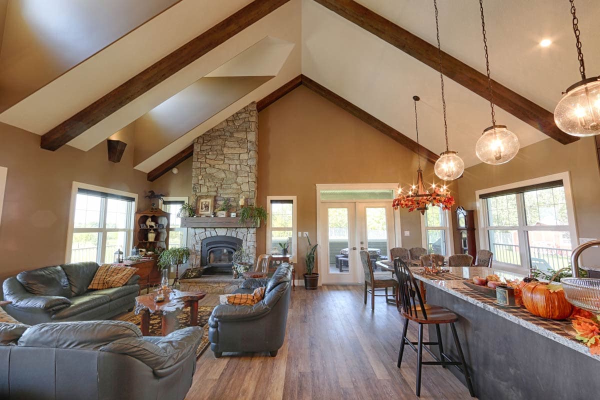 Great room with vaulted ceiling, exposed beams, stone fireplace, kitchen island, and dining area.
