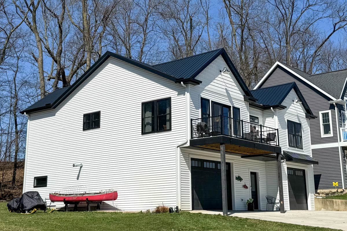Modern Farmhouse house plan exterior, two stories, white siding, black metal roof, gabled dormers, balcony, and attached garages.