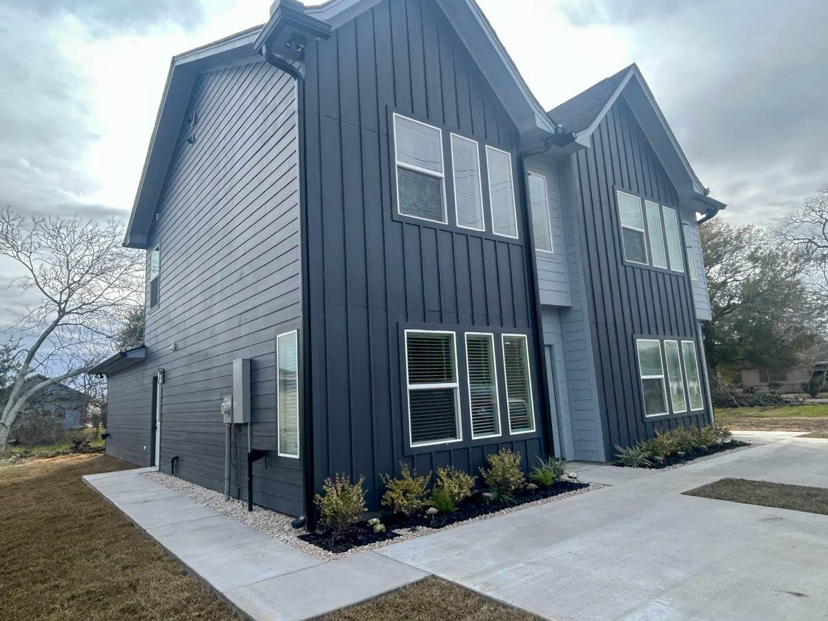 Modern house plan exterior with dark vertical siding, multiple gables, and numerous tall windows.