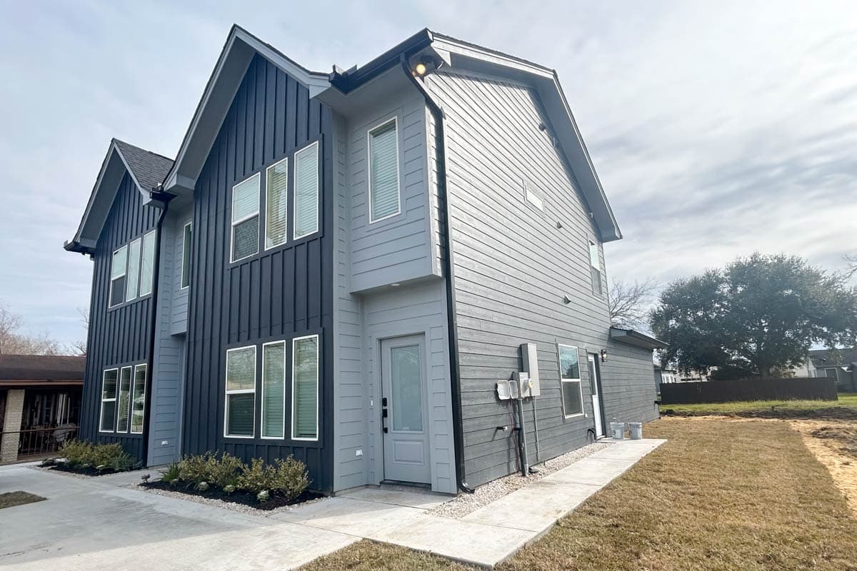 Modern two-story house plan exterior with vertical dark gray siding, horizontal light gray siding, and prominent gables.