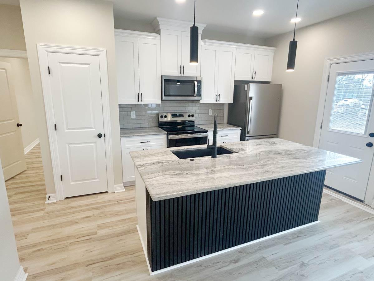 Kitchen with white cabinets, granite countertops, central island with black slatted base, stainless steel appliances, and adjacent doorway.