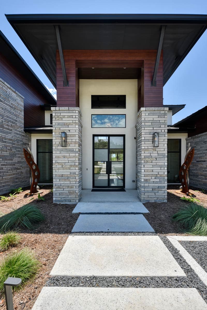 Modern house plan exterior with stacked stone columns, wood accents, large windows, and a geometric glass front door.