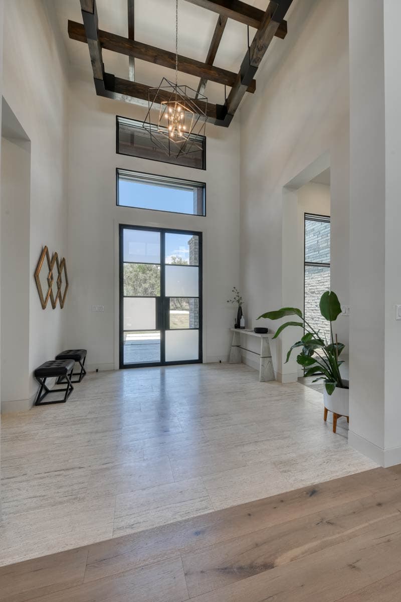 Interior foyer with vaulted ceiling, exposed wood beams, large glass door, and modern chandelier.