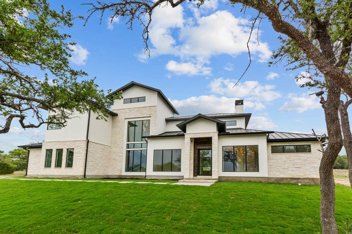 House plan exterior. Modern style, two-story home with a stone and stucco facade. Features include a flat roof, large windows, and a covered entry.