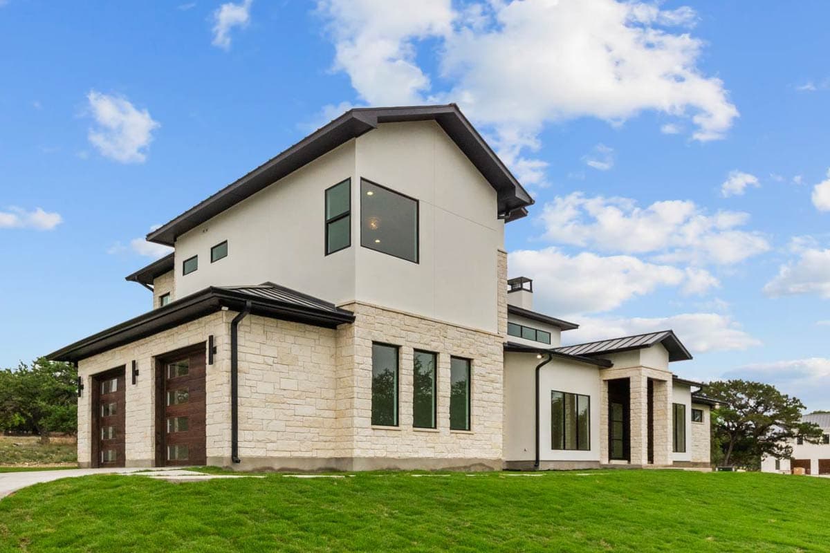 Modern two-story house plan exterior with stucco and stone, asymmetrical gables, and a multi-paneled garage door.