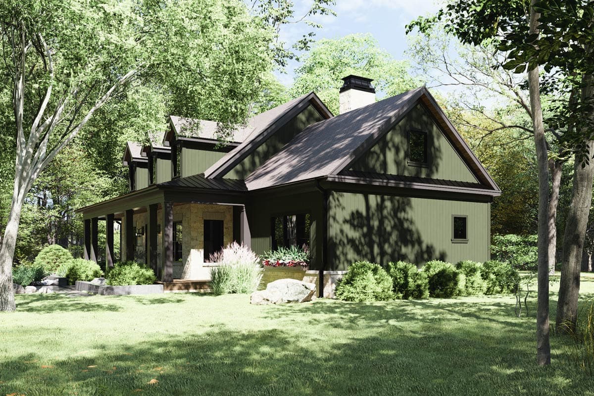 A green-sided house with a dark roof and trim sits amidst trees. A covered porch and stone accents add charm to the home in a natural setting.