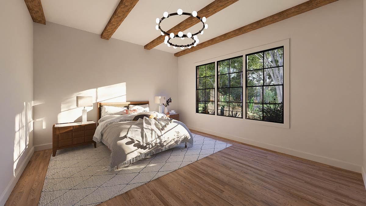 A sunlit bedroom with a cozy bed, geometric rug, and a large window looking out onto greenery, with modern light fixtures.