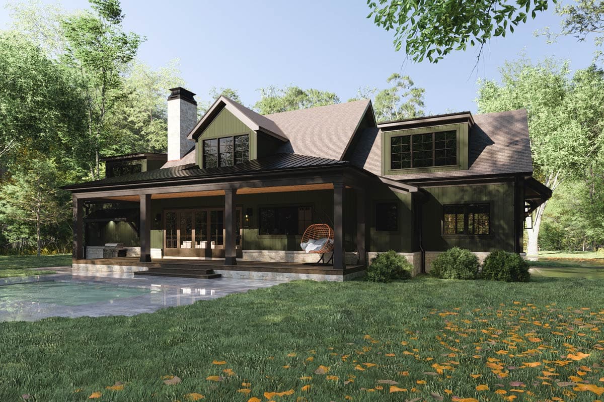 A modern dark green house with a large covered porch, an outdoor pool, and a hanging chair, set in a wooded area on a sunny day.