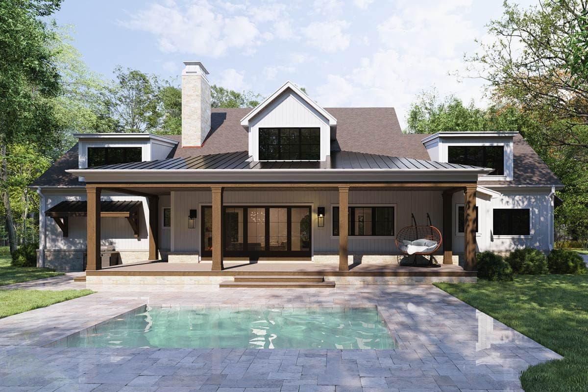 A modern farmhouse with a porch and pool. The house has a white exterior, dark windows, and a chimney. A stone patio surrounds the pool.