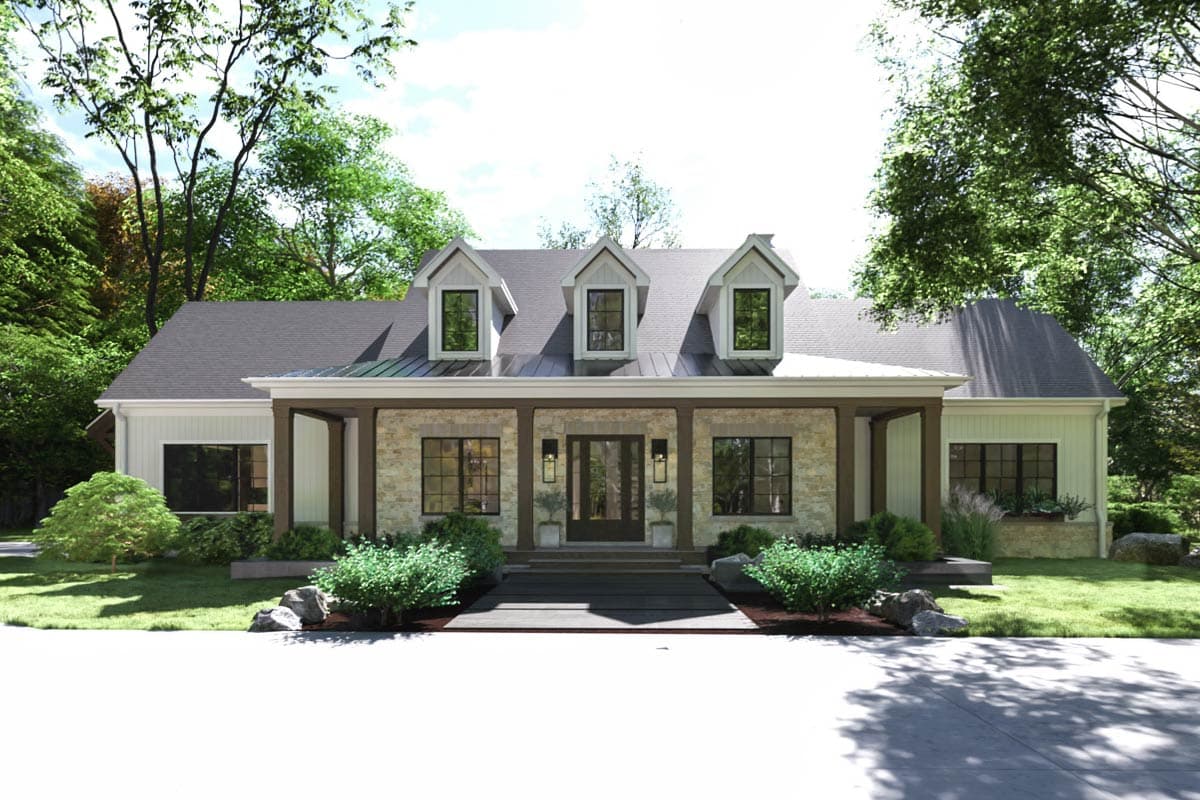A farmhouse-style home with three dormers, stone and white siding, and a covered porch. Lush greenery surrounds the house.