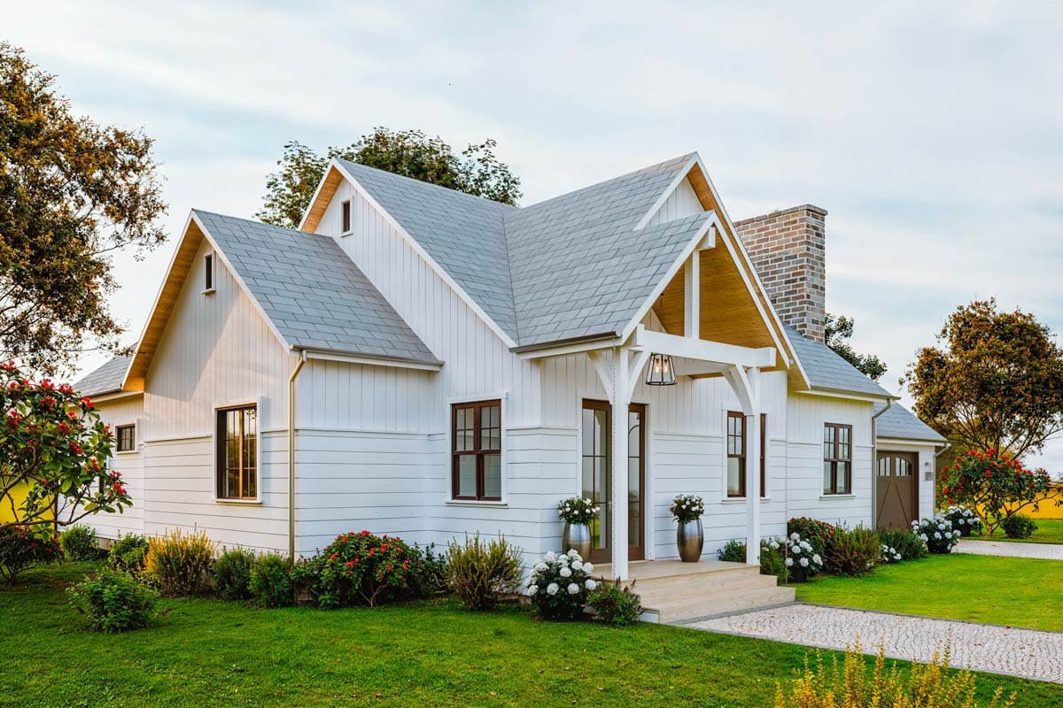 Modern farmhouse exterior with gabled rooflines, white board and batten siding, and a prominent brick chimney.