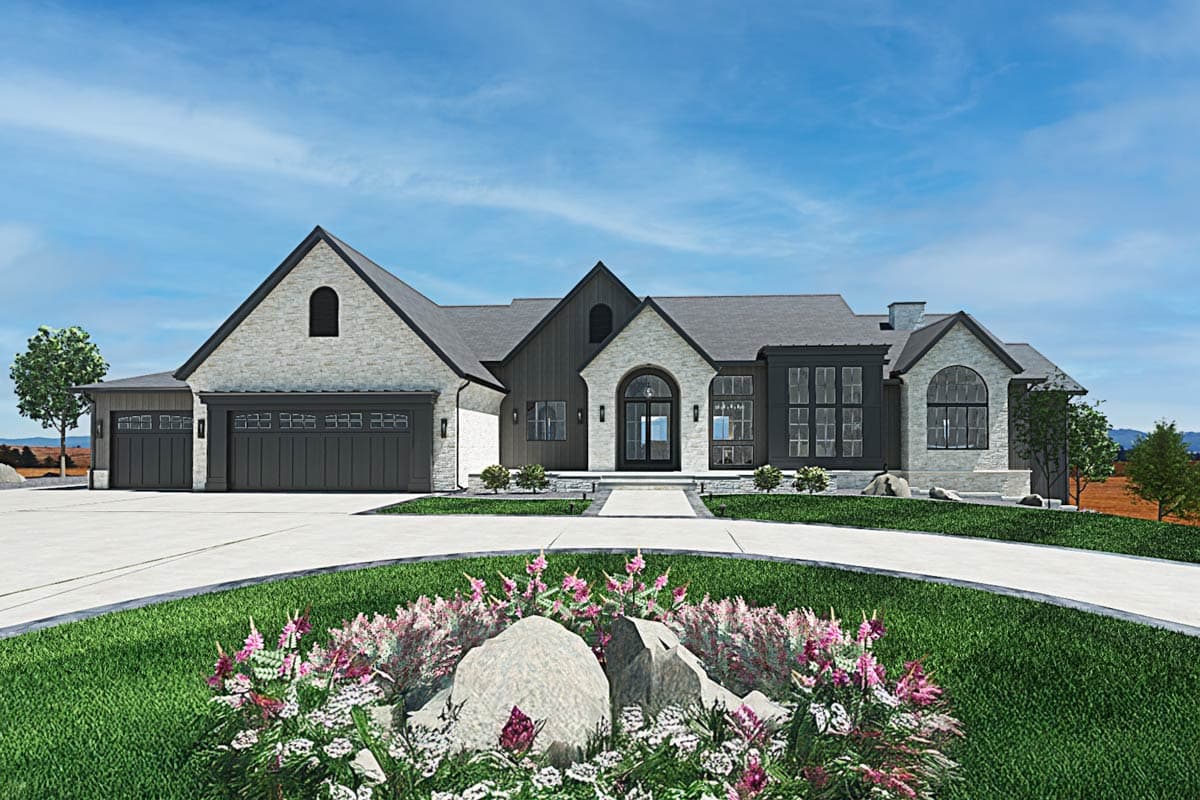 A modern, multi-gabled house with a stone and dark siding exterior, circular driveway, and vibrant landscaping under a blue sky.
