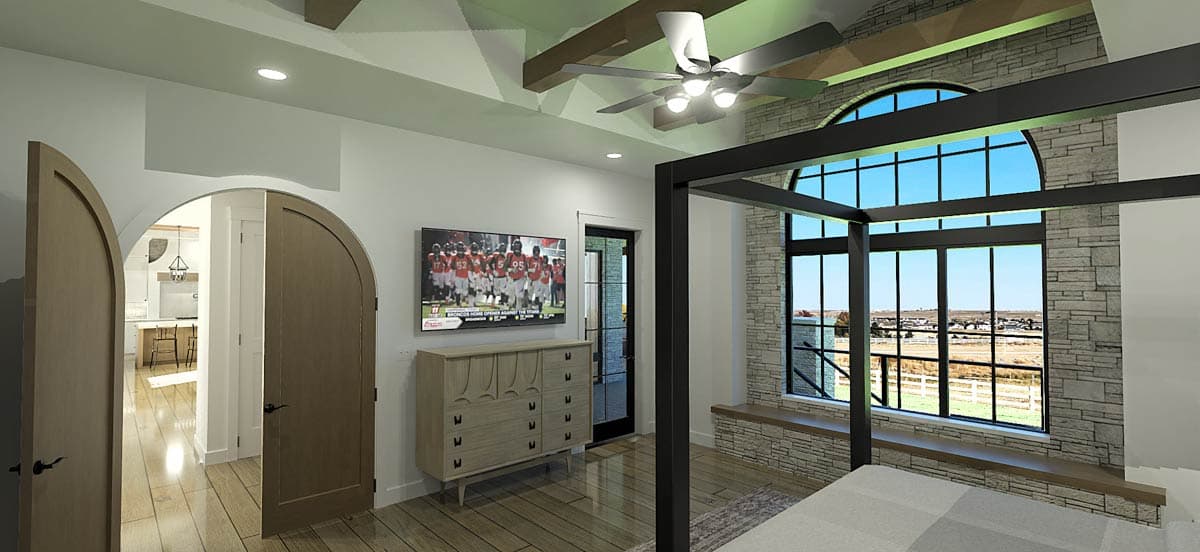 Spacious bedroom with a four-poster bed, large arched window, and a TV mounted on a dresser. Visible is an open archway leading to a kitchen.