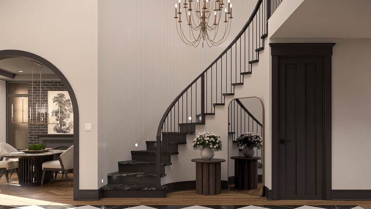 Interior view of a curved staircase with dark metal railings, a chandelier, and a tall paneled door.