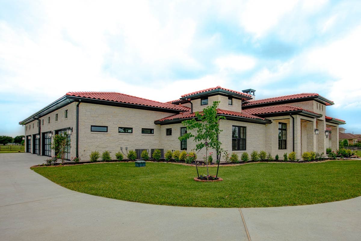 House plan exterior: Ranch style, stone facade, red tile roof, multiple garage doors, and covered entry.