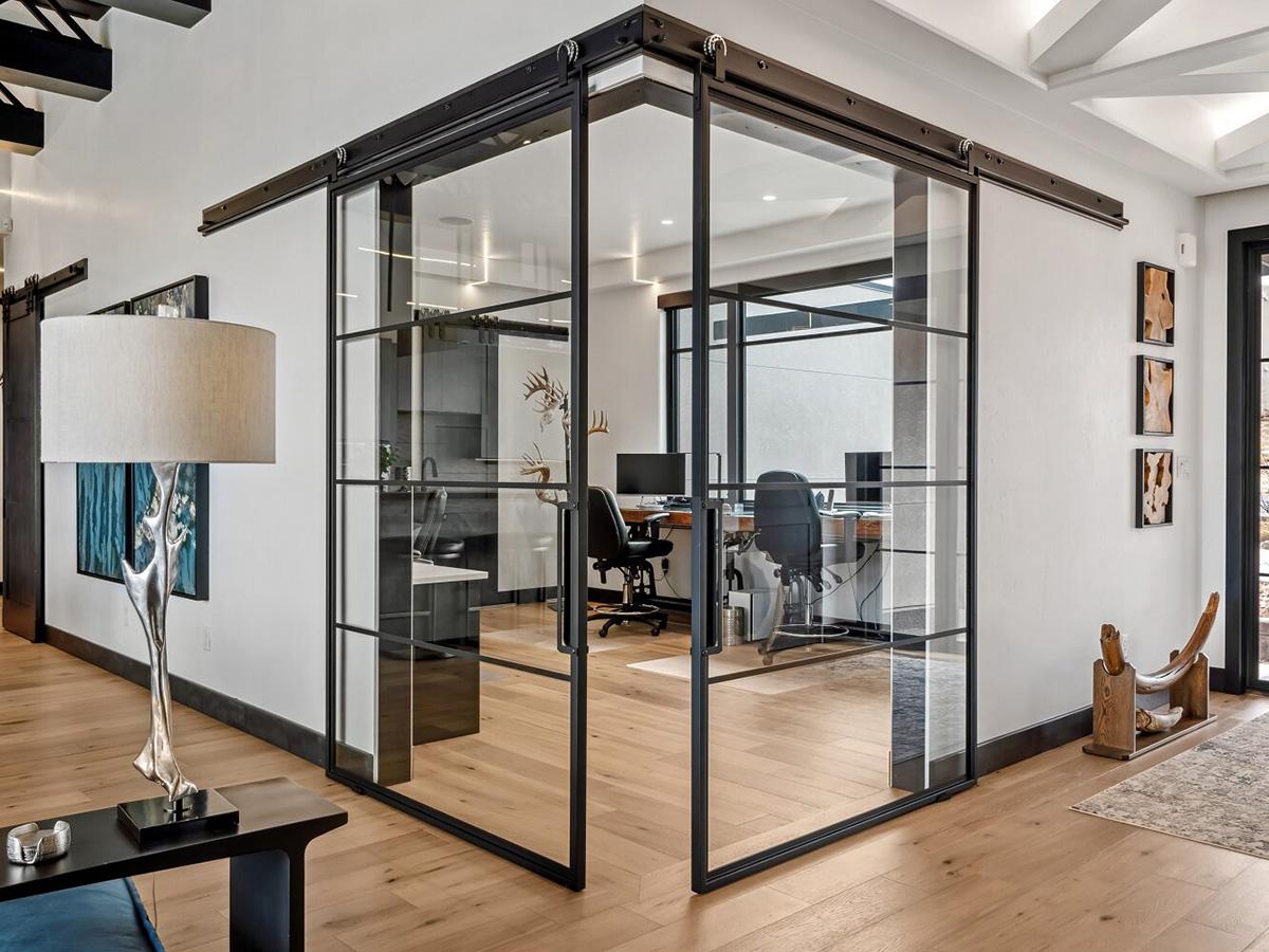 Modern office with glass walls, black metal frames, sliding barn door, and wood floors.
