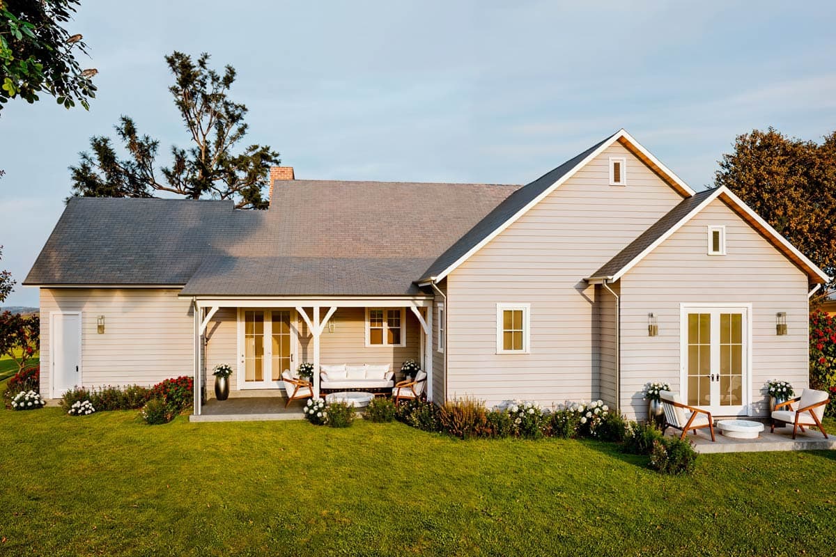 Exterior of a light gray farmhouse-style house with a covered porch and manicured lawn.