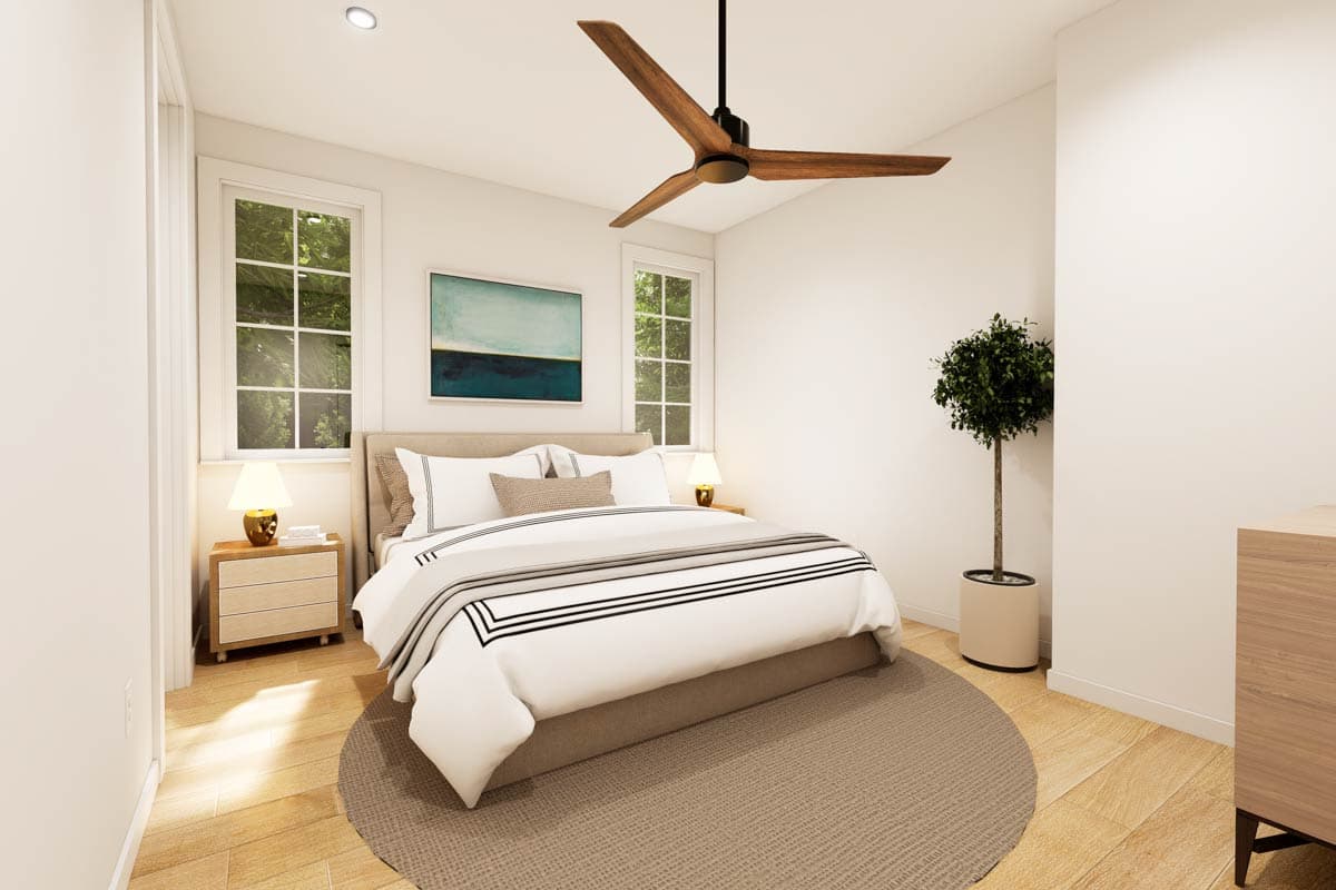 A modern bedroom with a bed, artwork, fan, and large windows offering views of nature.