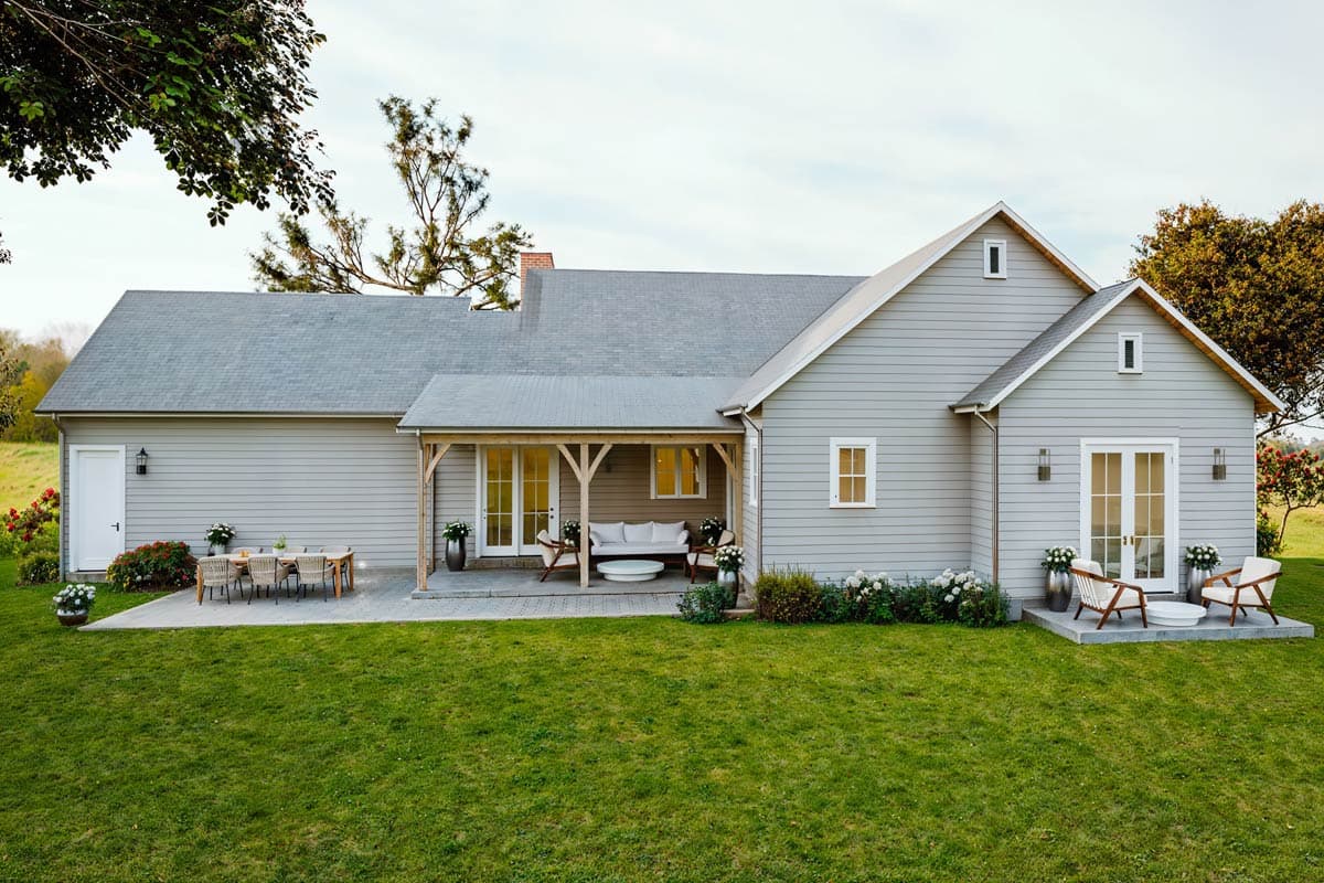House plan exterior: Single-story Modern Farmhouse with gabled roof, covered porch with wood posts, and patio with dining set.