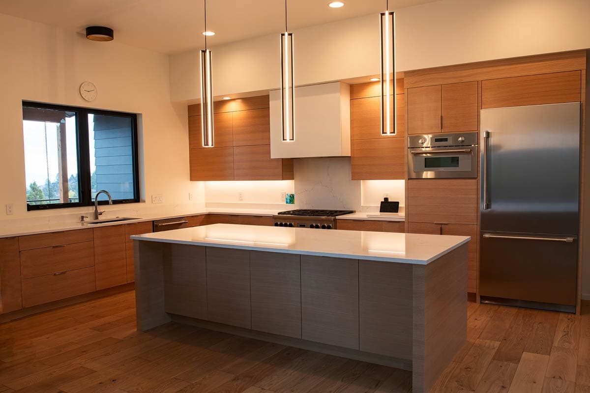 Modern kitchen with wood cabinetry, large island with waterfall countertop, stainless steel appliances, and pendant lighting.
