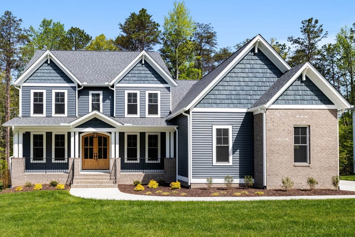 Two-story house plan exterior with prominent gables, covered front porch, shingle and lap siding, and brick accents.