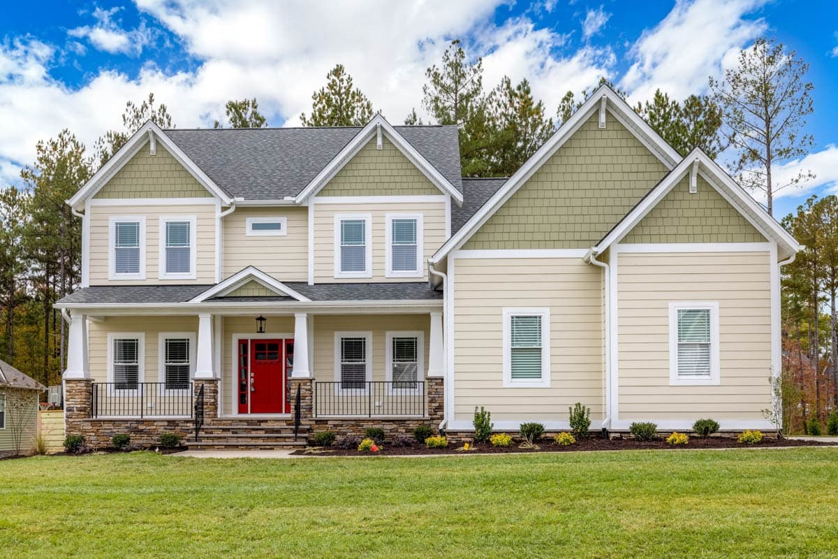 Two-story house plan exterior with a covered front porch, gables, dormers, and stone foundation.