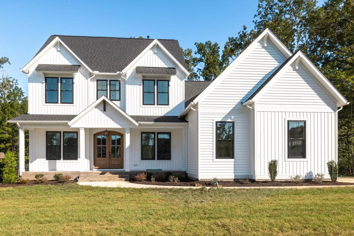 Modern Farmhouse house plan exterior with white board and batten siding, gable dormers, and a covered porch with arched double entry doors.