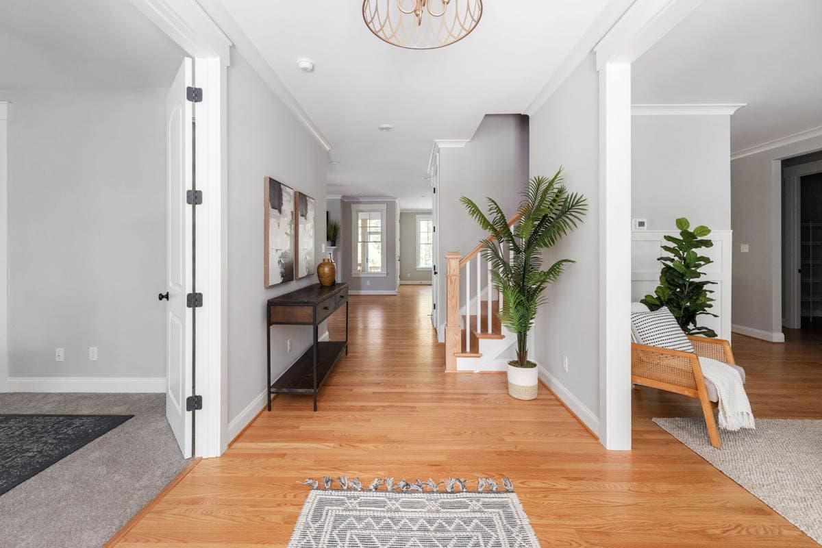 Interior view of a foyer with hardwood floors, staircase, console table, and open doorways to other rooms.