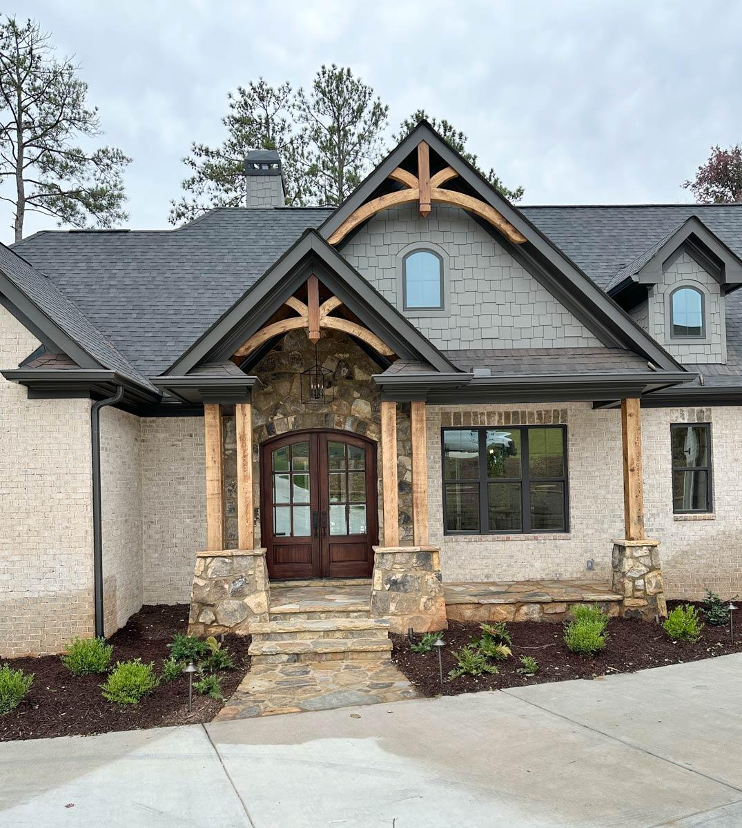 House plan exterior with stone-clad pillars supporting a porch with wood beams, double front doors, and arched dormer windows.