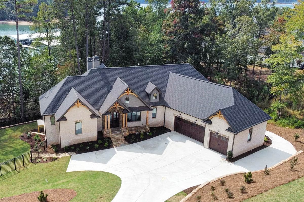 House plan exterior: Modern Farmhouse, one story, stone and brick facade, covered entry porch with timber beams, dormers, and three-car garage.